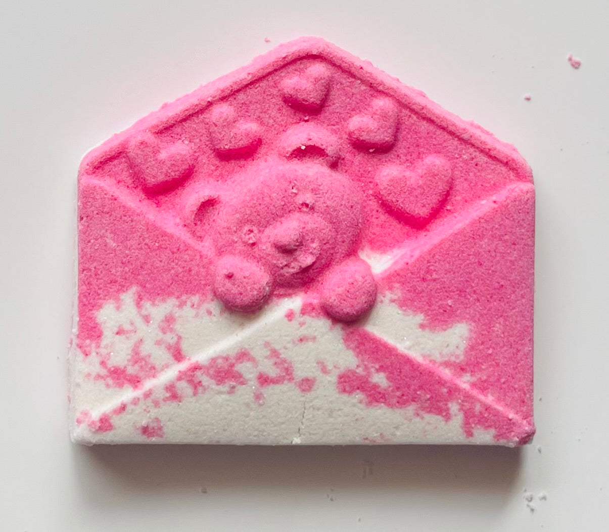 Pink and white bath bomb shaped like a letter envelope on a light background